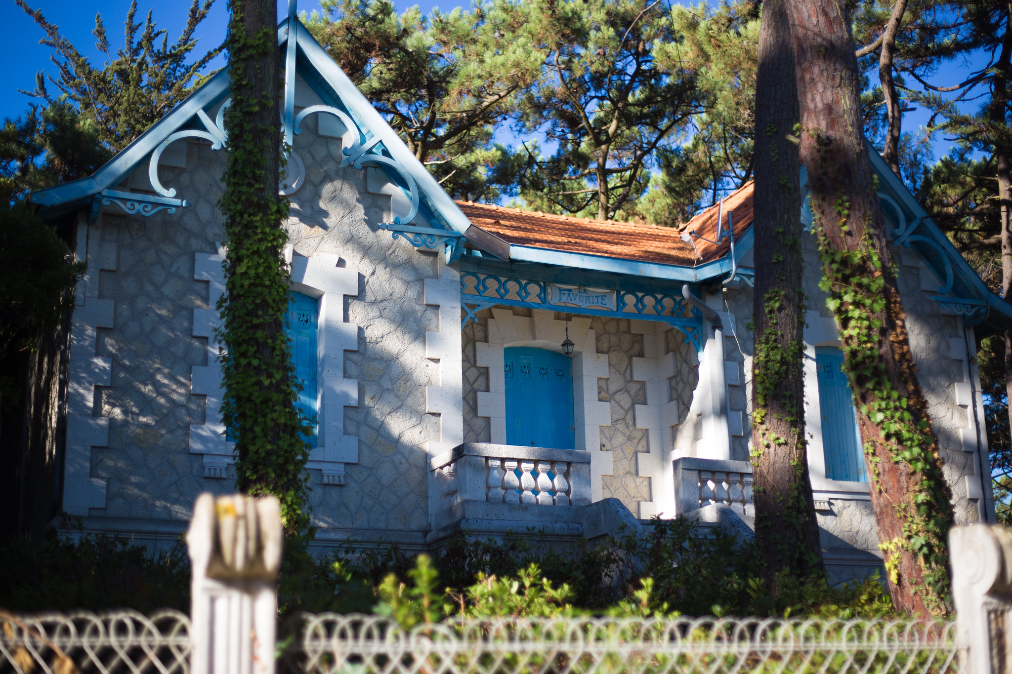 Petite chapelle blanche et bleue de style Art nouveau entourée de grands pins, avec détails architecturaux ornementaux et lierre grimpant, à Bordeaux.