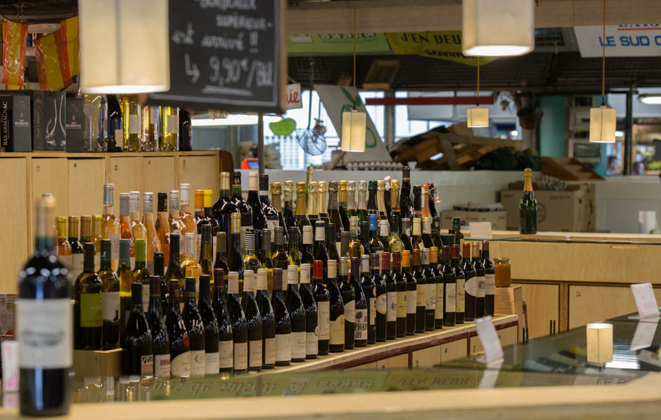 Vitrine d'une cave à vin bordelaise présentant plusieurs rangées de bouteilles de vin rouge, blanc et rosé avec étiquettes visibles, dans un décor de magasin moderne avec comptoir en bois clair.