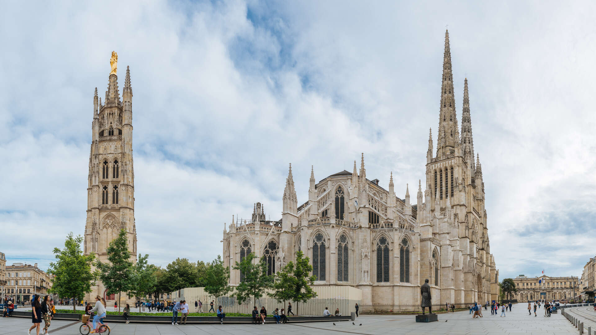 Vue de la Cathédrale Saint-André et de la Tour Pey Berland à Bordeaux, avec leurs flèches gothiques caractéristiques, entourées de bâtiments historiques et d'une place publique.