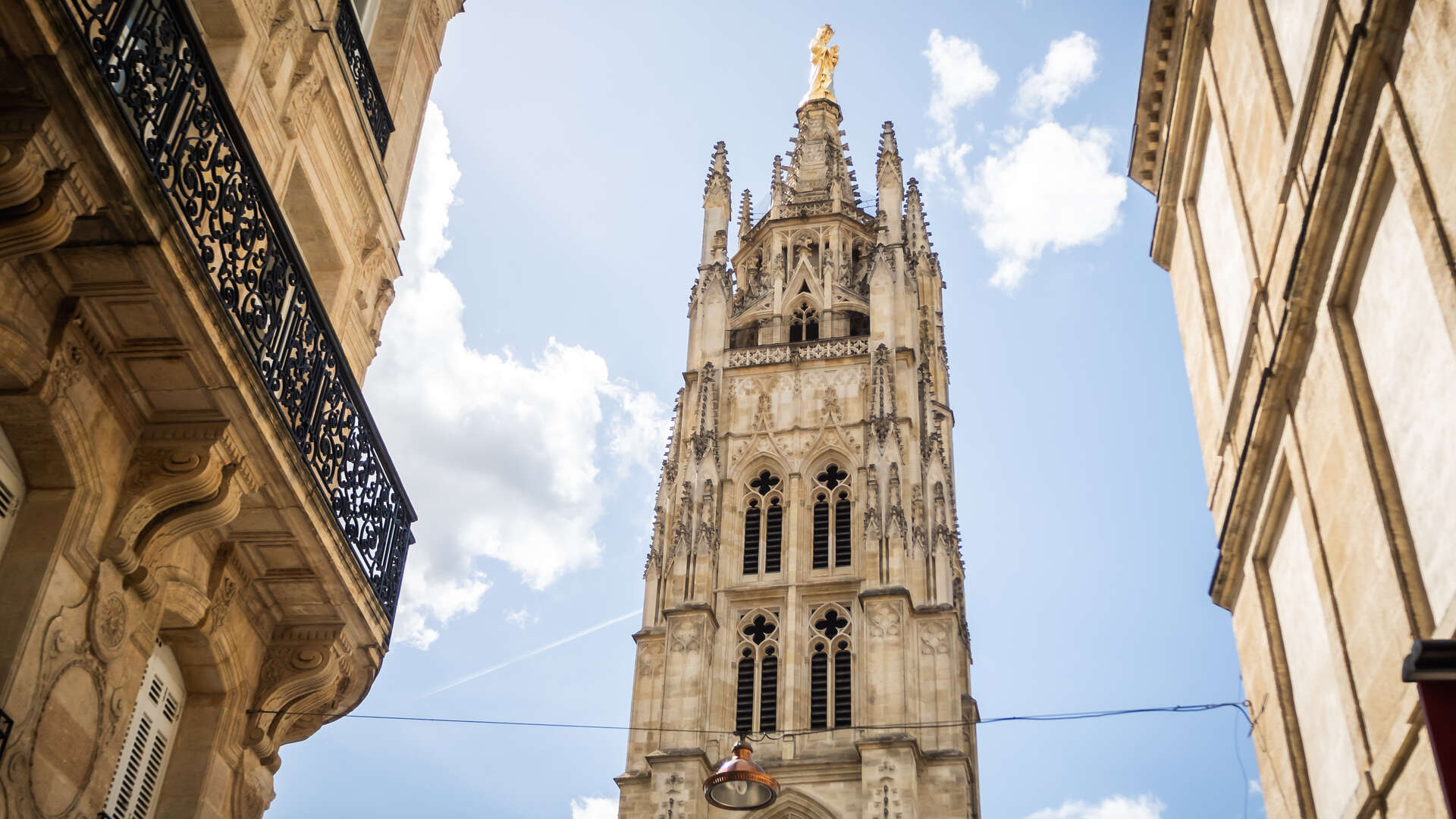 La Tour Pey Berland, clocher gothique de la Cathédrale Saint-André de Bordeaux, vue depuis une rue étroite avec façades haussmanniennes de part et d'autre.