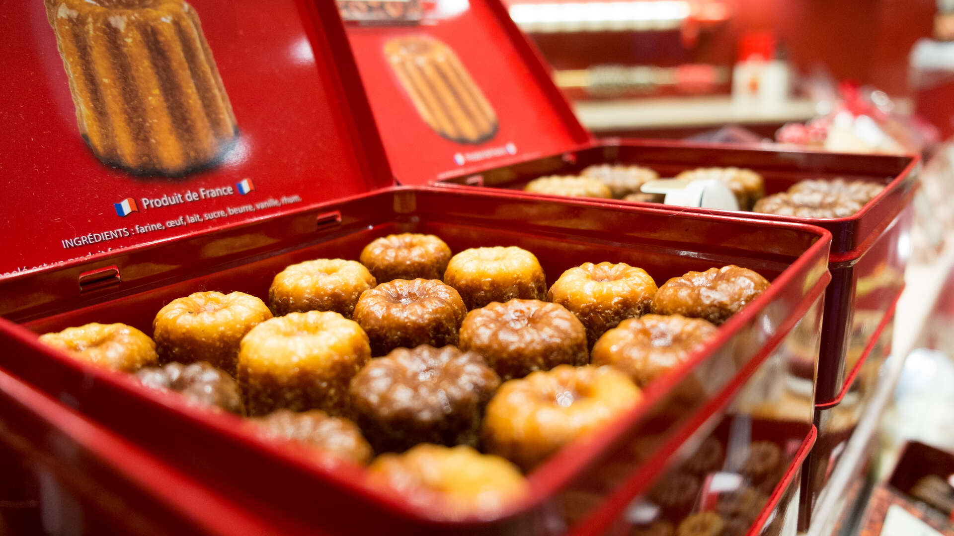 Boîte rouge ouverte contenant des canelés bordelais dorés saupoudrés de sucre, produit français traditionnel de Bordeaux