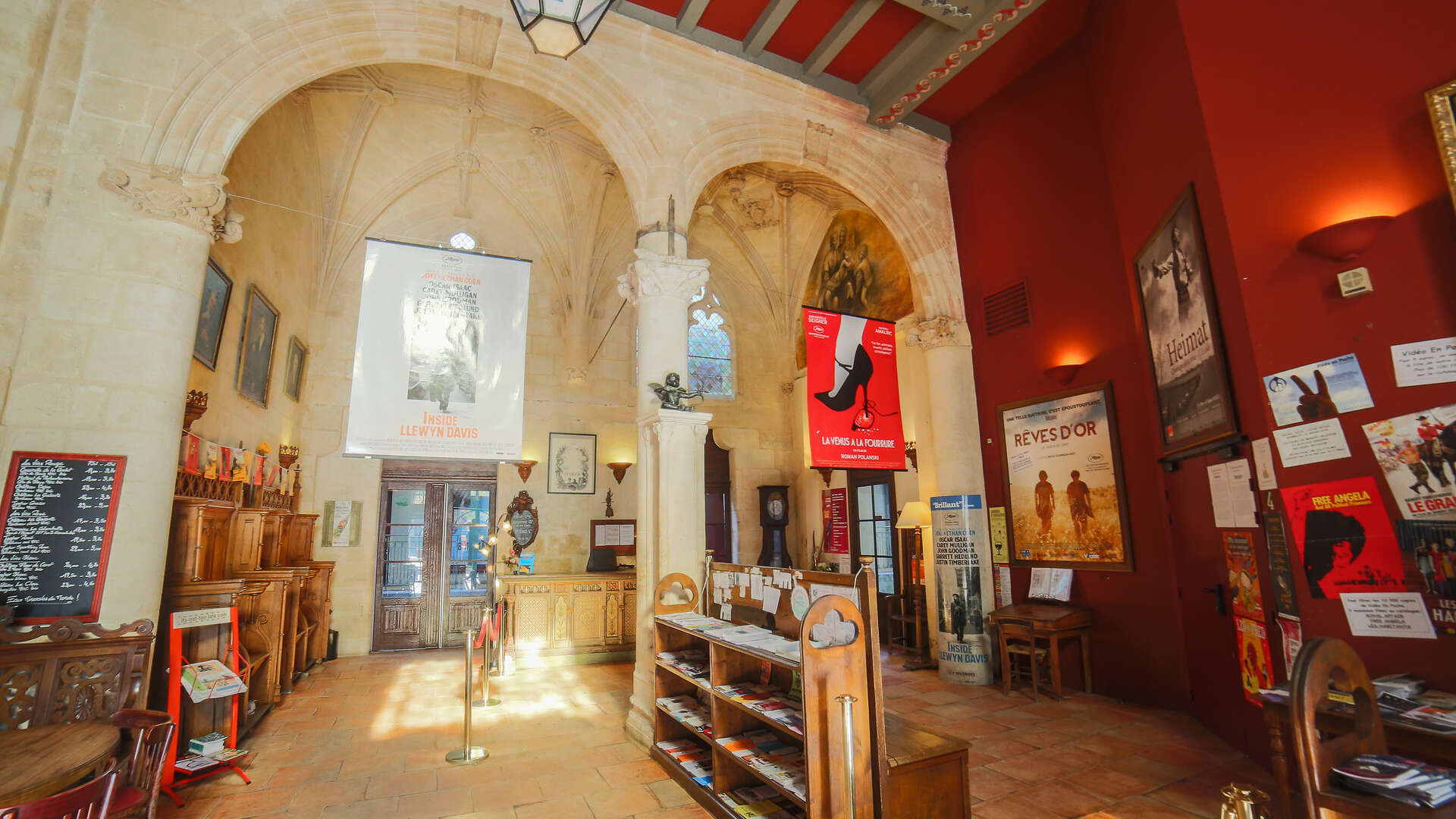 Intérieur du cinéma Utopia à Bordeaux, avec voûtes en pierre, murs rouges, affiches de films et mobilier en bois dans une ancienne chapelle.