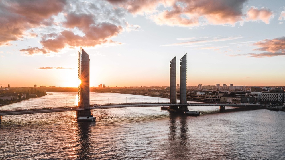 Vue aérienne du Pont Chaban-Delmas à Bordeaux au coucher de soleil, avec ses deux tours verticales caractéristiques enjambant la Garonne, la ville en arrière-plan.