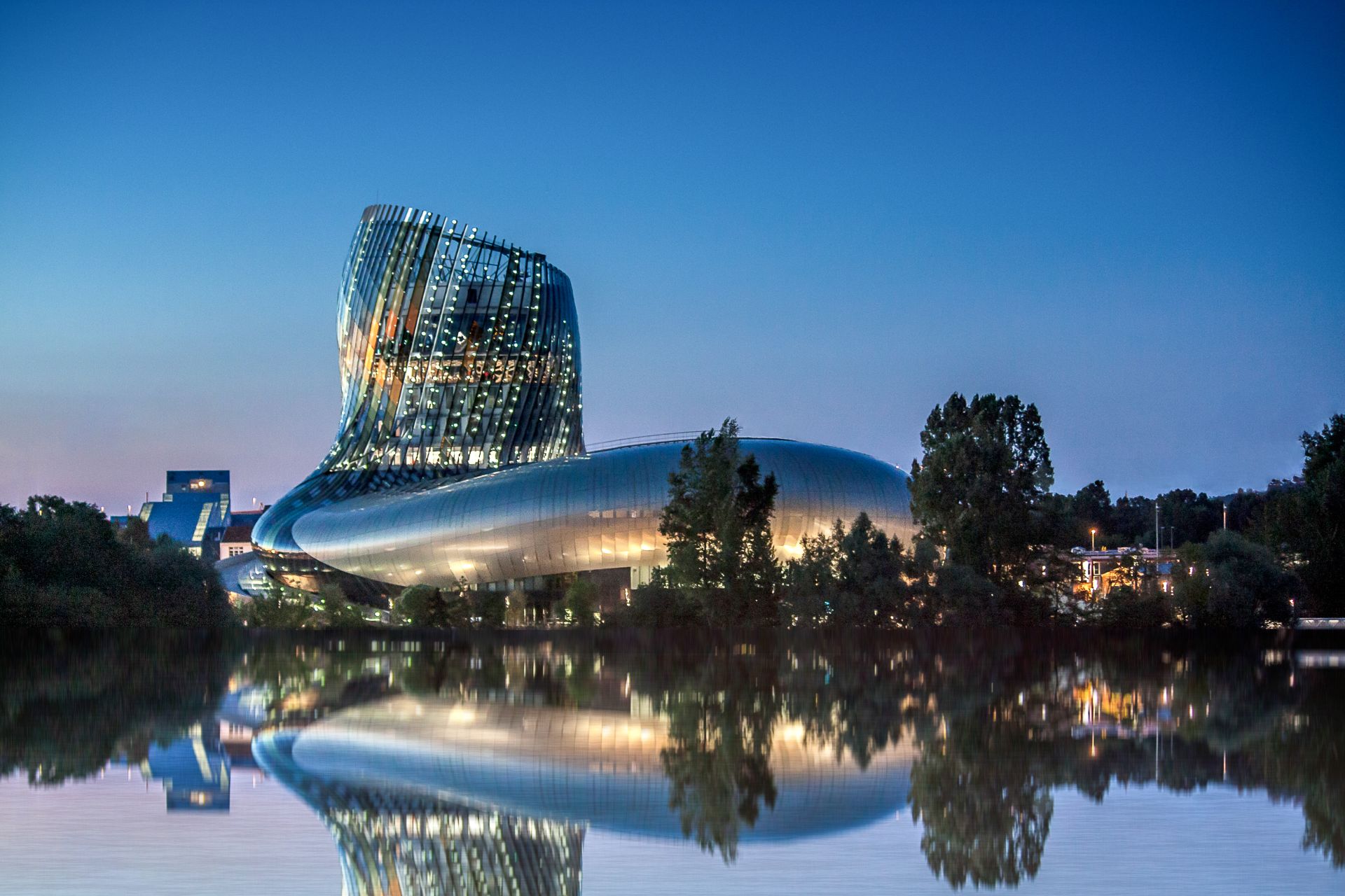La Cité du Vin à Bordeaux, bâtiment architectural moderne avec façade inclinée illuminée, reflet dans l'eau calme au crépuscule