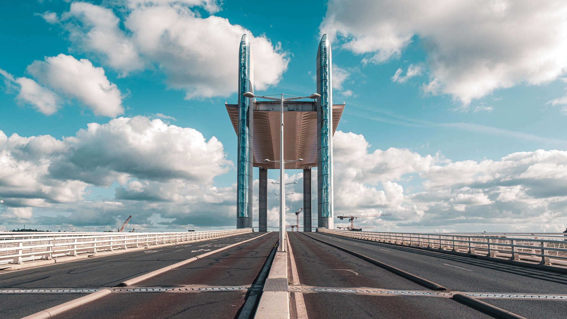 Vue perspective du Pont de Pierre de Bordeaux avec ses deux tours caractéristiques en verre bleu-vert, sous un ciel nuageux bleu clair