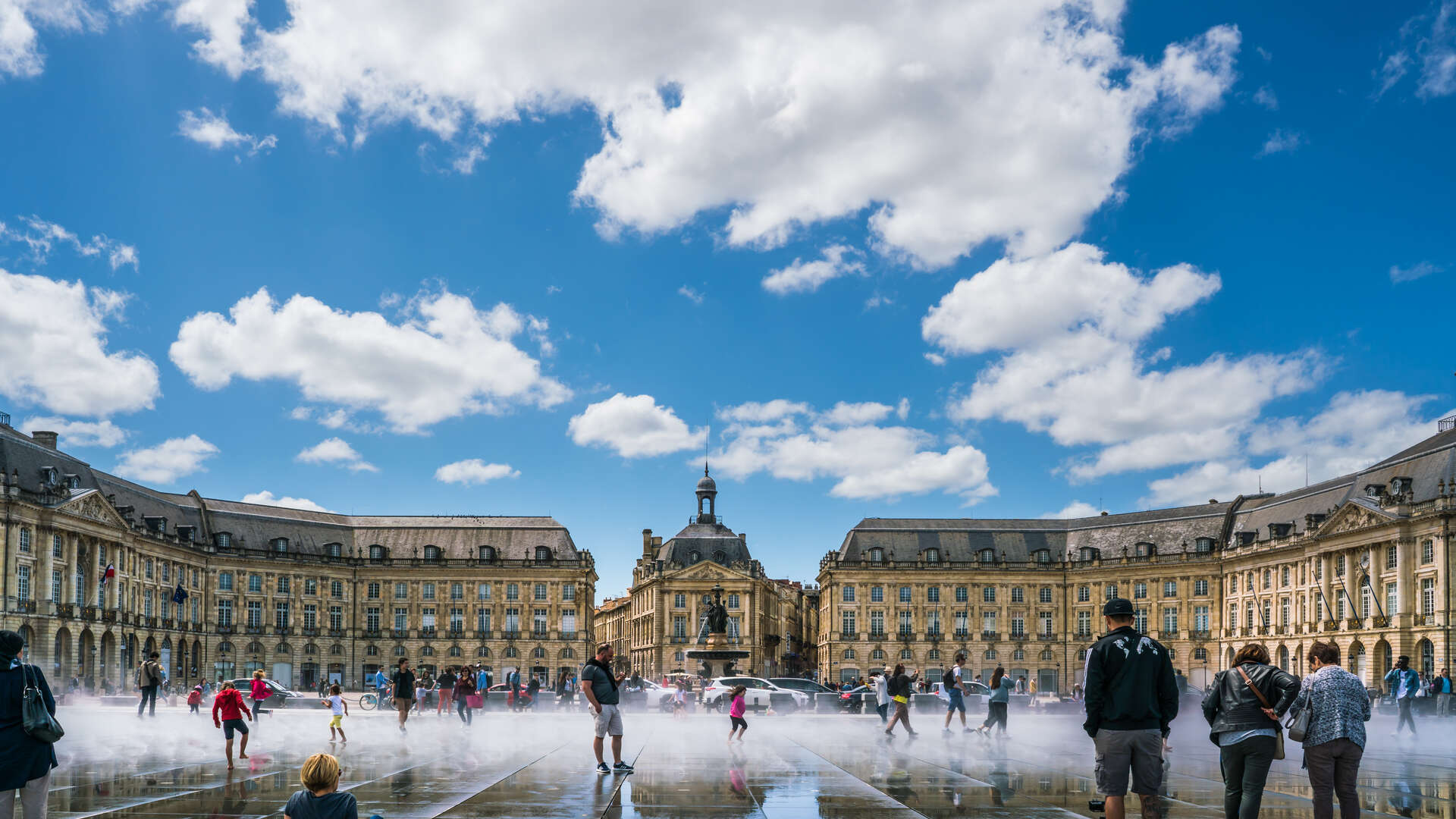Place de la Bourse à Bordeaux avec fontaine miroir, bâtiments classiques en pierre dorée et visiteurs par beau temps