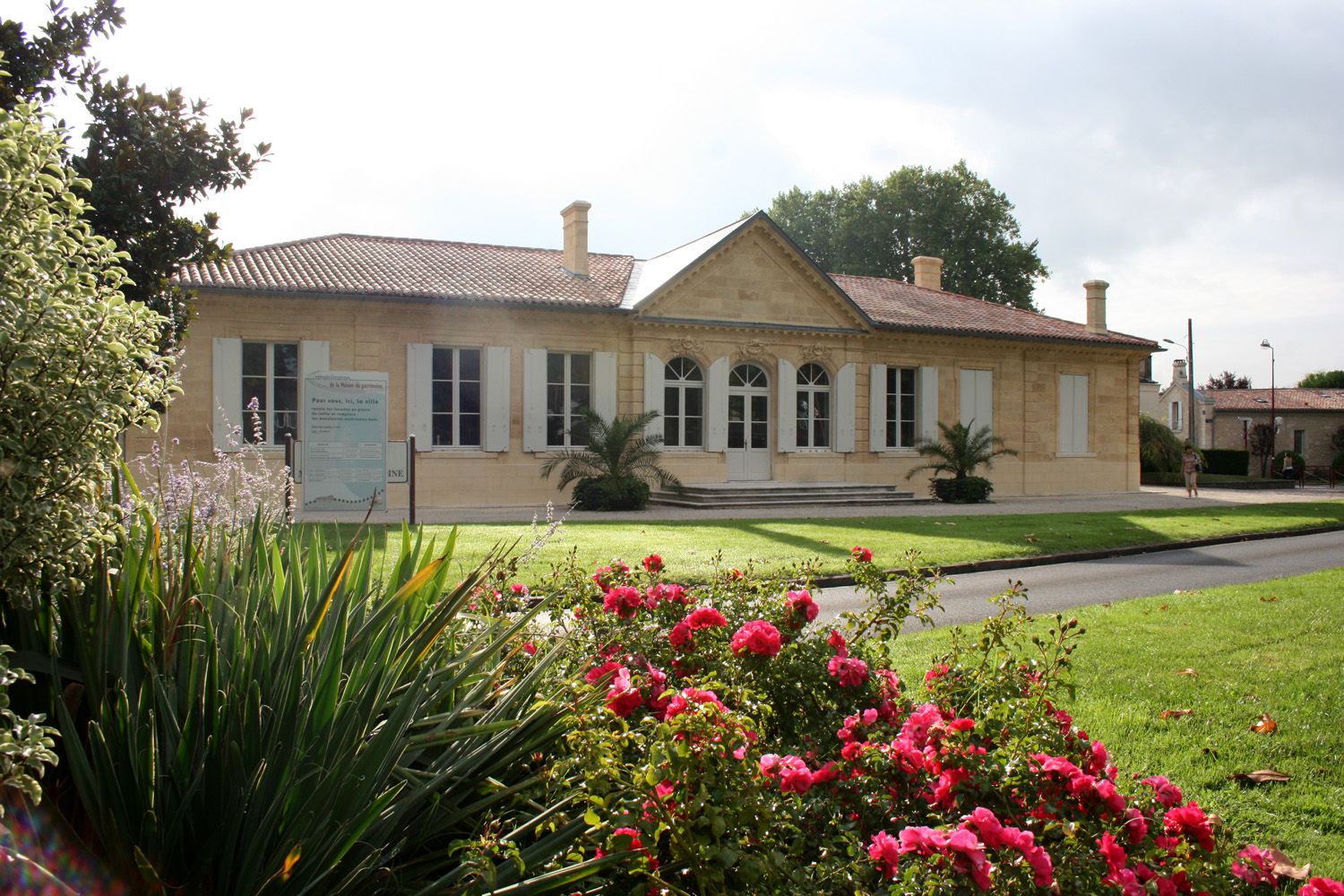 Bâtiment architectural de style néoclassique à Bordeaux, avec façade en pierre beige, colonnes blanches et roses rouges en parterre