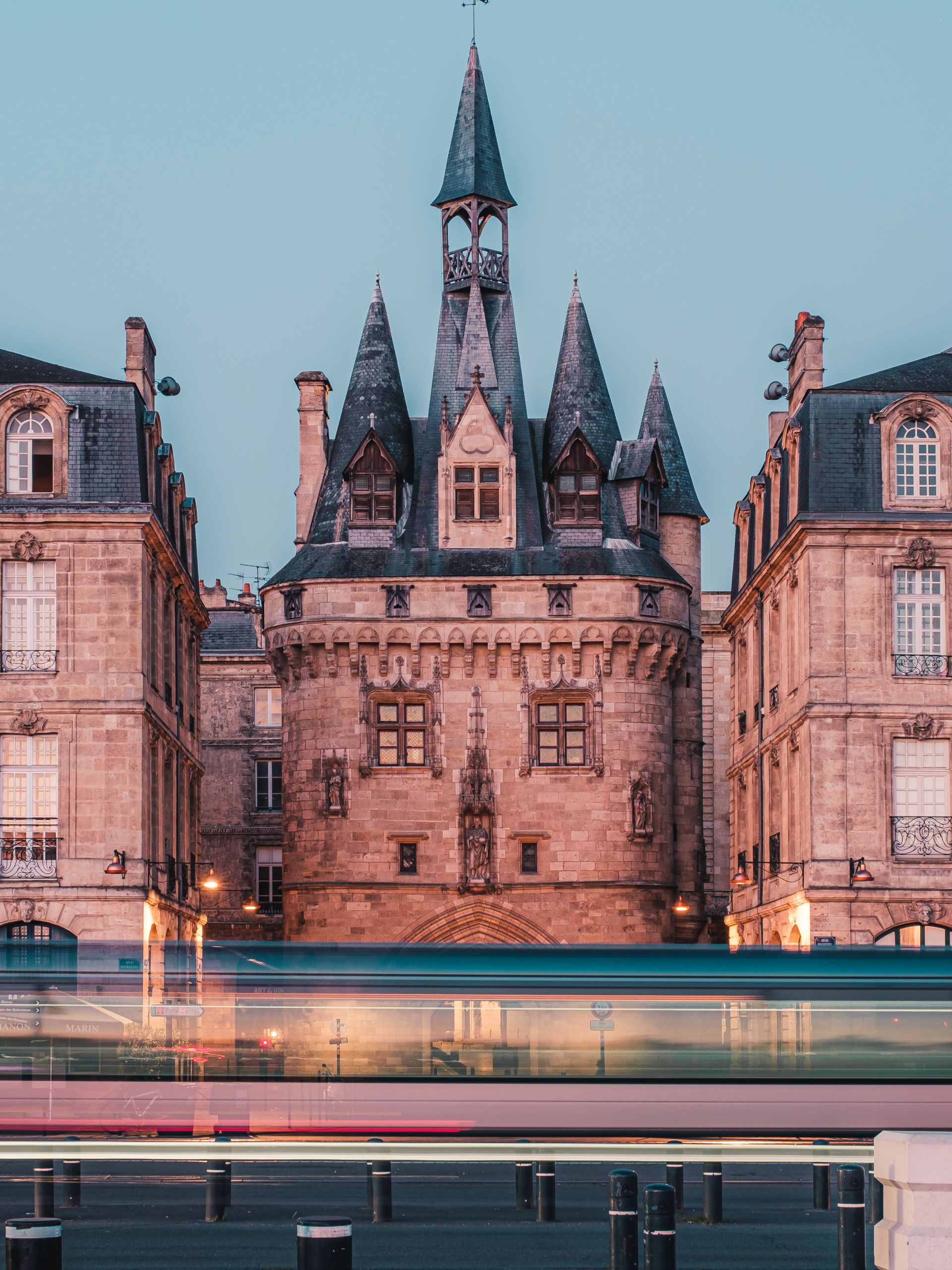 Château de la Malartrie à Bordeaux avec ses tours pointues en pierre rose illuminées au crépuscule, flanqué de bâtiments mansardés et reflété dans l'eau