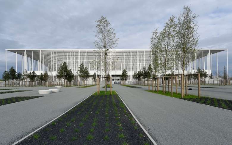 Vue architecturale d'un bâtiment moderne aux façades de métal blanc ajouré, avec une allée centrale plantée d'arbres et de zones vertes, situé à Bordeaux.