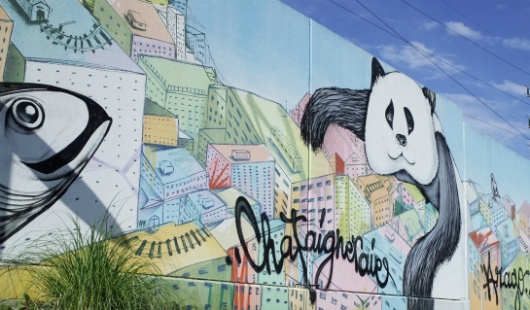 Fresque murale colorée à Bordeaux représentant des visages stylisés, des motifs géométriques et du texte artistique sur un bâtiment urbain.