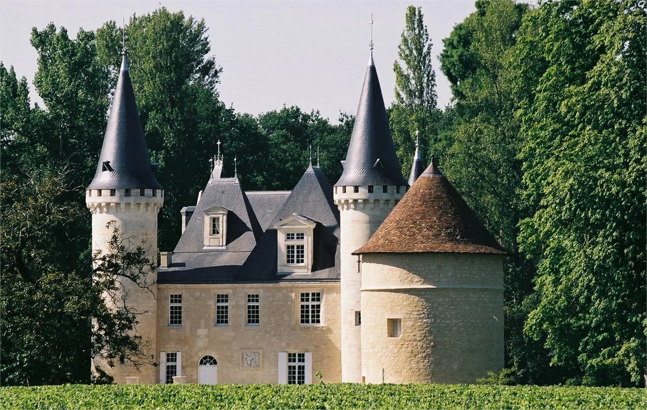 Château médiéval avec tours pointues et toits coniques, entouré de verdure près de Bordeaux