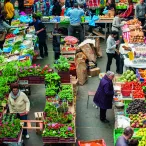 Vue aérienne d'un marché couvert à Bordeaux avec des étals de fruits et légumes frais colorés, des vendeurs et des clients circulant entre les présentoirs de produits locaux.