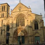 Église gothique de Bordeaux avec façade en pierre blonde, tour carrée, grandes baies vitrées et portail en arche ogivale, entourée de bâtiments historiques.