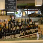 Vitrine d'une cave à vin bordelaise présentant plusieurs rangées de bouteilles de vin rouge, blanc et rosé avec étiquettes visibles, dans un décor de magasin moderne avec comptoir en bois clair.