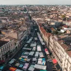 Vue aérienne d'une rue de Bordeaux avec un marché aux puces et antiquaires, montrant des étals avec des auvents colorés entourés de bâtiments haussmanniens et de toitures en tuiles rouges.
