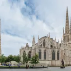 Vue de la Cathédrale Saint-André et de la Tour Pey Berland à Bordeaux, avec leurs flèches gothiques caractéristiques, entourées de bâtiments historiques et d'une place publique.