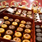 Assortiment de cannelés bordelais et autres pâtisseries fines présentés dans des boîtes rouges avec étiquettes, exposés en vitrine de pâtisserie.