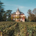 Château viticole en briques rouges avec tourelle et toit pointu, entouré de vignobles en automne près de Bordeaux