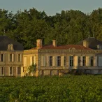 Château bordelais du XVIIIe siècle avec façade en pierre de taille, toits mansardés et dômes, entouré de vignobles et d'arbres