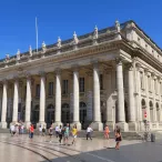 Le Grand Théâtre de Bordeaux avec sa façade néoclassique majestueuse, ses colonnes blanches imposantes et sa terrasse devant remplie de visiteurs par une journée ensoleillée.