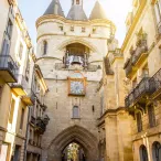 La Grosse Cloche de Bordeaux, tour médiévale du XVe siècle avec ses deux tourelles coniques, son horloge et sa cloche, encadrée par des bâtiments historiques en pierre de taille dans une ruelle pavée.
