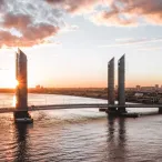 Vue aérienne du Pont Chaban-Delmas à Bordeaux au coucher de soleil, avec ses deux tours verticales caractéristiques enjambant la Garonne, la ville en arrière-plan.