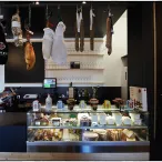 Devanture d'une charcuterie bordelaise avec jambon ibérique suspendu, vitrine réfrigérée contenant charcuteries et fromages, menu affiché au mur listant les assortiments et spécialités régionales.
