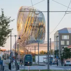 Vue urbaine de Bordeaux avec un tramway moderne passant devant le bâtiment architecturale en verre courbé de la Cité du Vin, entouré de bâtiments historiques et de lignes électriques de tramway.