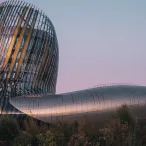 La Cité du Vin à Bordeaux, bâtiment architectural moderne avec une tour inclinée en verre et métal aux reflets dorés, surplombant une structure horizontale cylindrique, photographié au crépuscule.