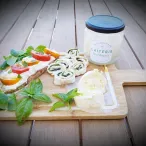 Plateau de dégustation avec pain grillé garni de fromage blanc et légumes frais, rouleaux de mozzarella aux herbes, pot de Laiterie Burdigala, et feuilles de basilic frais sur une planche en bois