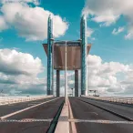 Vue perspective du Pont de Pierre de Bordeaux avec ses deux tours caractéristiques en verre bleu-vert, sous un ciel nuageux bleu clair