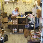 Boutique de décoration intérieure à Bordeaux avec une femme travaillant à son comptoir, entourée de paniers, textiles, objets de décoration et mobilier artisanal.