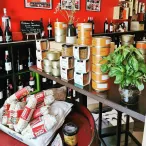 Intérieur d'une boutique bordelaise présentant des vins, des conserves de pâtés et terrines, des boîtes de foie gras dorées, des bouteilles de vin exposées sur les murs rouges, et des produits régionaux du sud-ouest français.