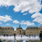 Place de la Bourse à Bordeaux avec fontaine miroir, bâtiments classiques en pierre dorée et visiteurs par beau temps