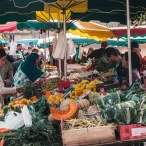 Marché en plein air à Bordeaux avec vendeurs et clients sous des parasols colorés verts, jaunes et rouges, étalant des fruits et légumes frais dont des courges, poivrons, carottes et légumes verts.