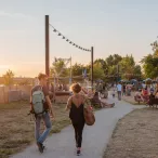 Deux jeunes femmes courent sur un sentier dans un parc urbain au coucher du soleil, avec des installations de jeux et des visiteurs en arrière-plan au Parc aux Angéliques de Bordeaux.