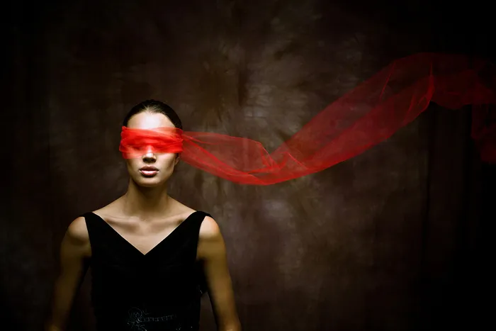 Femme les yeux bandés d'un tissu rouge flottant, portant une robe noire sur fond sombre, évoquant l'opéra La Fiancée du tsar de Bordeaux