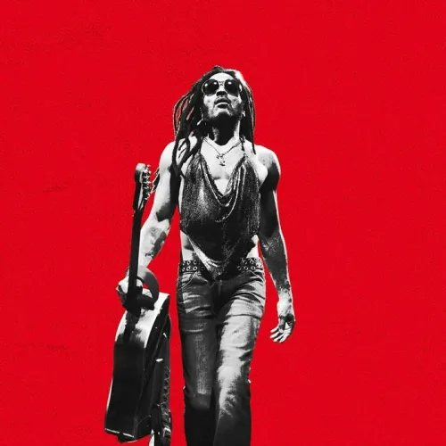 Lenny Kravitz en concert à l'Arkéa Arena de Bordeaux, portant des lunettes de soleil et tenant une guitare, sur fond rouge éclatant.