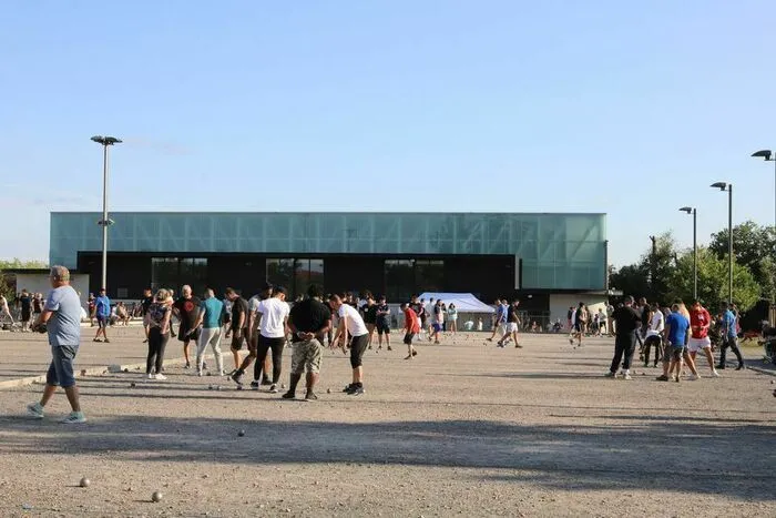 Vue d'une grande esplanade à Bordeaux avec une foule de participants et spectateurs rassemblés devant un bâtiment moderne aux façades vertes et noires lors d'un concours de pétanque.