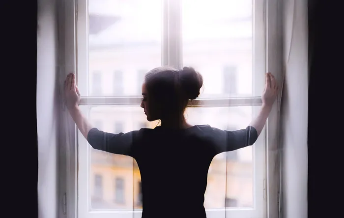 Silhouette d'une femme de dos, les bras écartés, regardant par une grande fenêtre avec vue sur la ville de Bordeaux