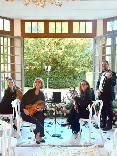 Quatre musiciens jouant du violon et un chanteur dans une salle lumineuse avec de grandes portes-fenêtres ouvertes sur un jardin verdoyant, lors d'un concert Minute Concerts à Bordeaux.