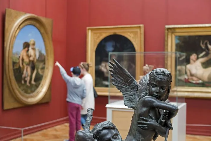 Intérieur du Musée des Beaux Arts de Bordeaux avec une sculpture d'ange en bronze au premier plan et une visiteure photographiant les peintures sur les murs rouges.
