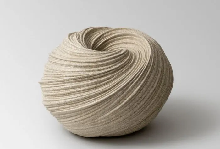 Sculpture céramique de forme sphérique avec des lignes ondulantes gravées, de couleur beige clair, présentée sur fond blanc