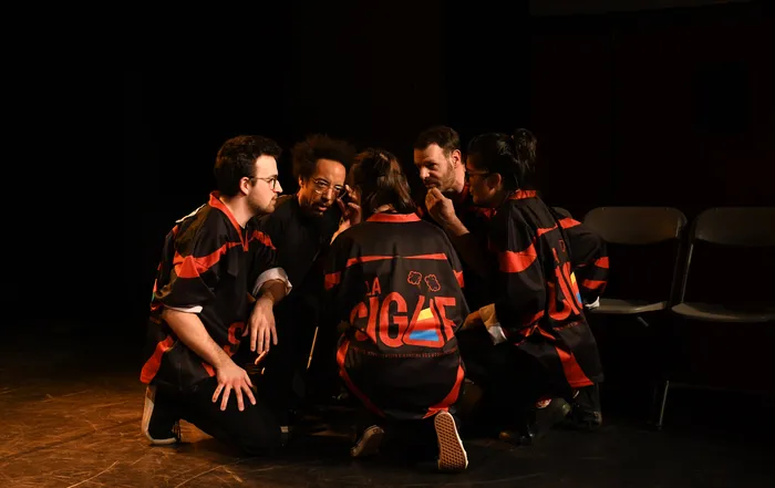 Groupe de six improvisateurs en tenue noire et rouge assis en cercle sur scène lors d'un match d'improvisation théâtrale à Bordeaux