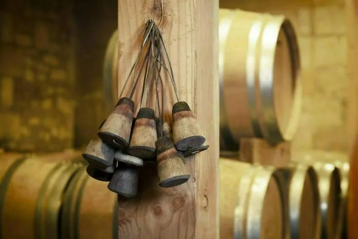 Clochettes de vendangeur suspendues à une poutre en bois dans une cave avec tonneaux de vin en arrière-plan, lors des Portes ouvertes aux châteaux de Castillon Côtes de Bordeaux