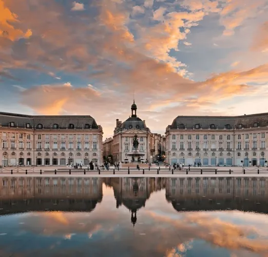 Place de la Bourse à Bordeaux avec le Miroir d'Eau reflétant les bâtiments historiques et le ciel au coucher de soleil