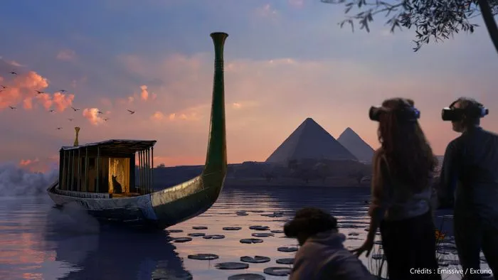 Vue immersive d'une exposition montrant une barque égyptienne stylisée sur l'eau, avec des pyramides en arrière-plan et des visiteurs observant la scène au coucher du soleil.