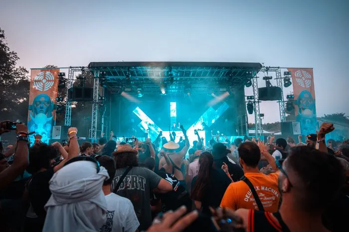 Foule de festivaliers devant une grande scène illuminée en bleu lors du festival Fort Décibel à Bordeaux, avec des mains levées et des téléphones pour filmer le spectacle.
