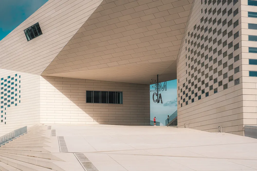 Vue extérieure de la MECA à Bordeaux, bâtiment contemporain en briques blanches avec architecture géométrique, esplanade pavée et bannière bleue