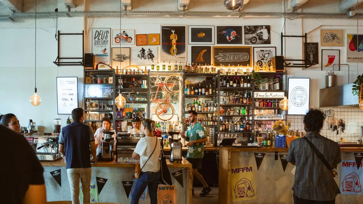 Intérieur d'un bar branché à Bordeaux avec un comptoir en bois, des étagères remplies de bouteilles de spiritueux, des vélos orange décorés au mur, et des clients servant à boire. Décoration murale avec cadres et affiches vintage.